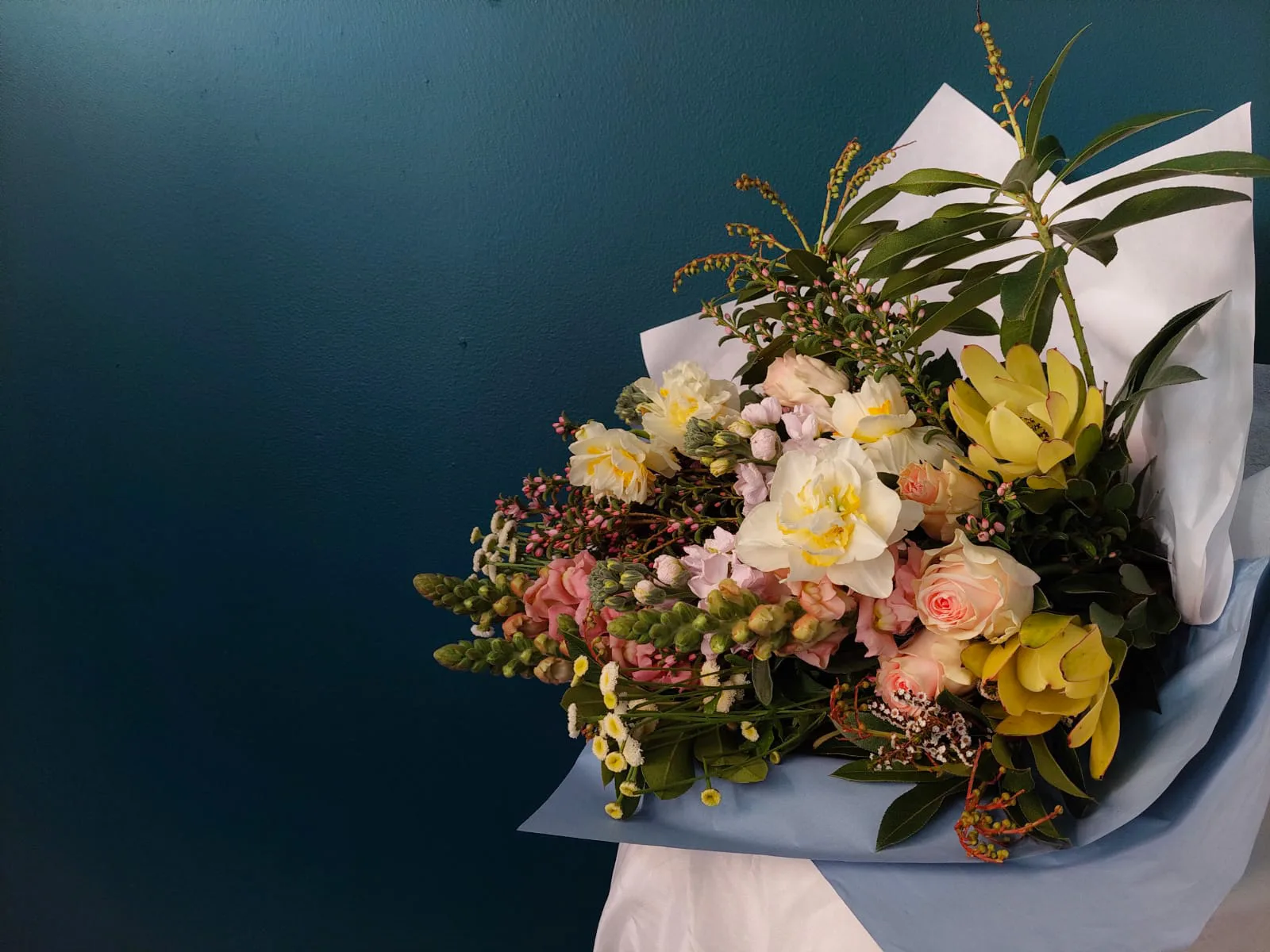Soft pastel spring bouquet photographed against the shop's deep-teal feature wall