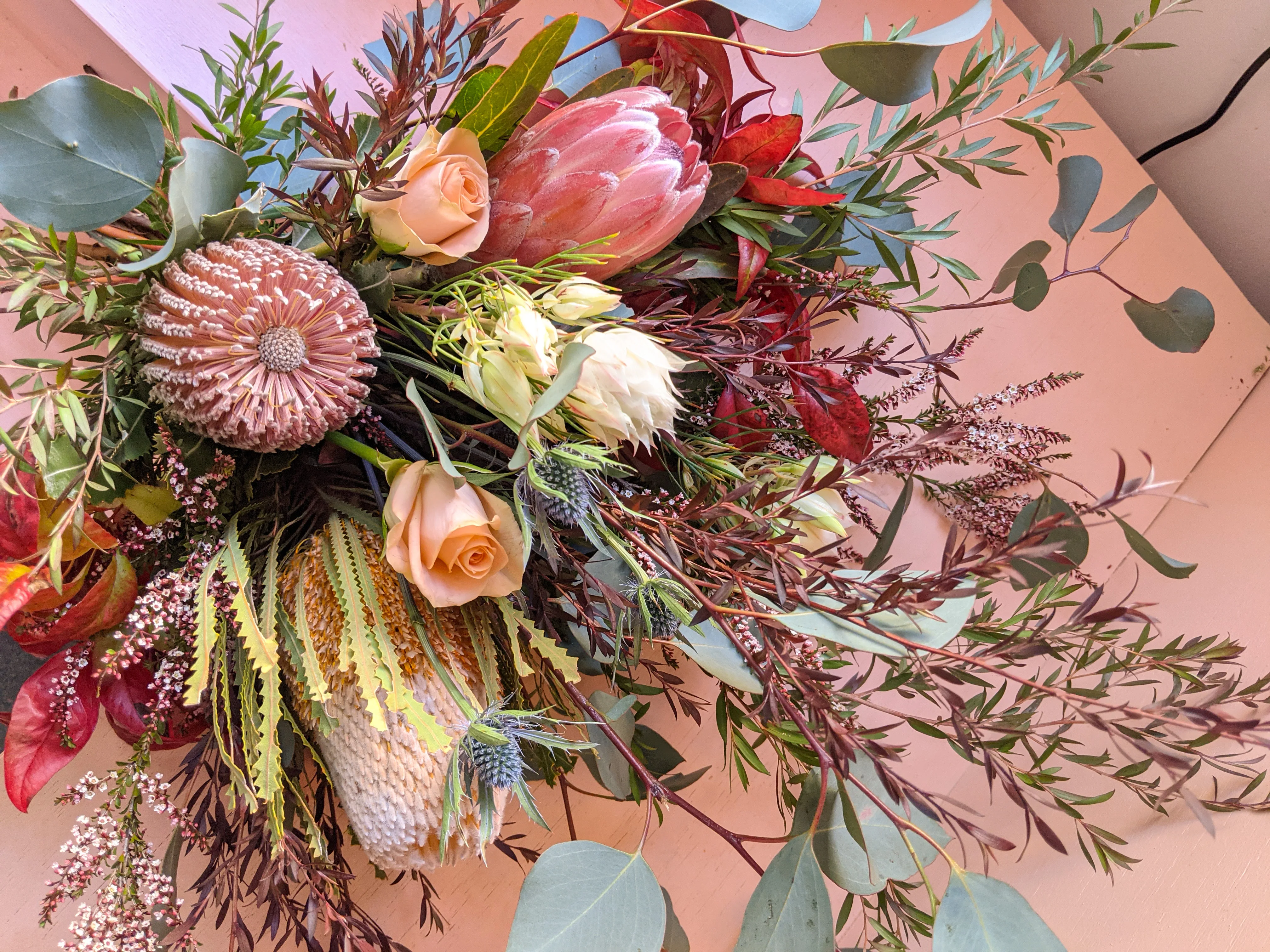 Native and textural flat-lay featuring king protea, banksia and blushing bride stems