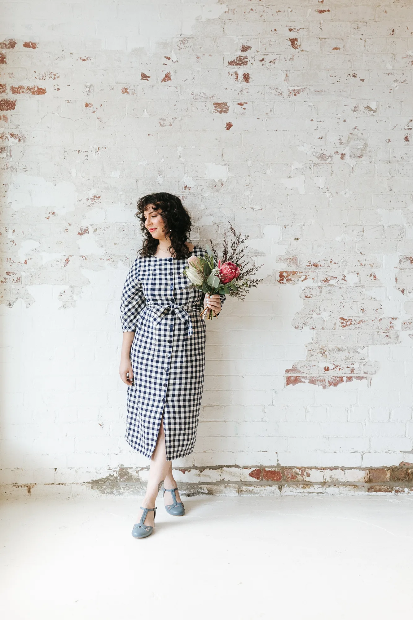 A Petal Pop florist holding a native protea posy against a whitewashed brick wall